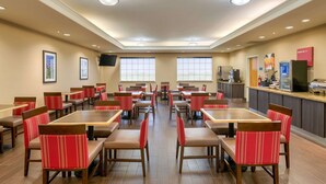 A hotel dining area with multiple tables and chairs, a kitchen counter, and framed pictures on the walls. - Comfort Inn & Suites, Odessa I-20 (Odessa)