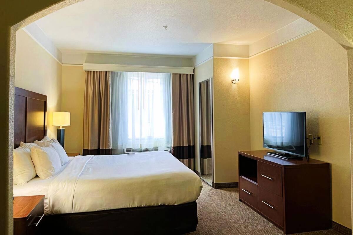 A hotel room with a bed, a television, a desk, and a window with curtains.