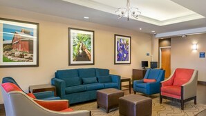 A hotel lobby with a blue sofa, a red armchair, and a blue armchair with a red cushion. There are framed pictures on the wall, a chandelier, and a television. - Comfort Inn & Suites, Odessa I-20 (Odessa)