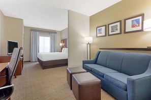 A hotel room with a bed, a blue sofa, a desk with a chair, a TV, and a lamp. - Comfort Suites West Dallas - Cockrell Hill (Dallas)