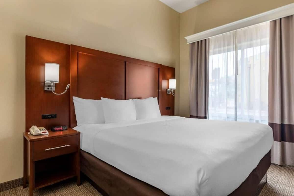 A hotel room with a large bed, bedside lamps, a nightstand with a phone, and a window with curtains.