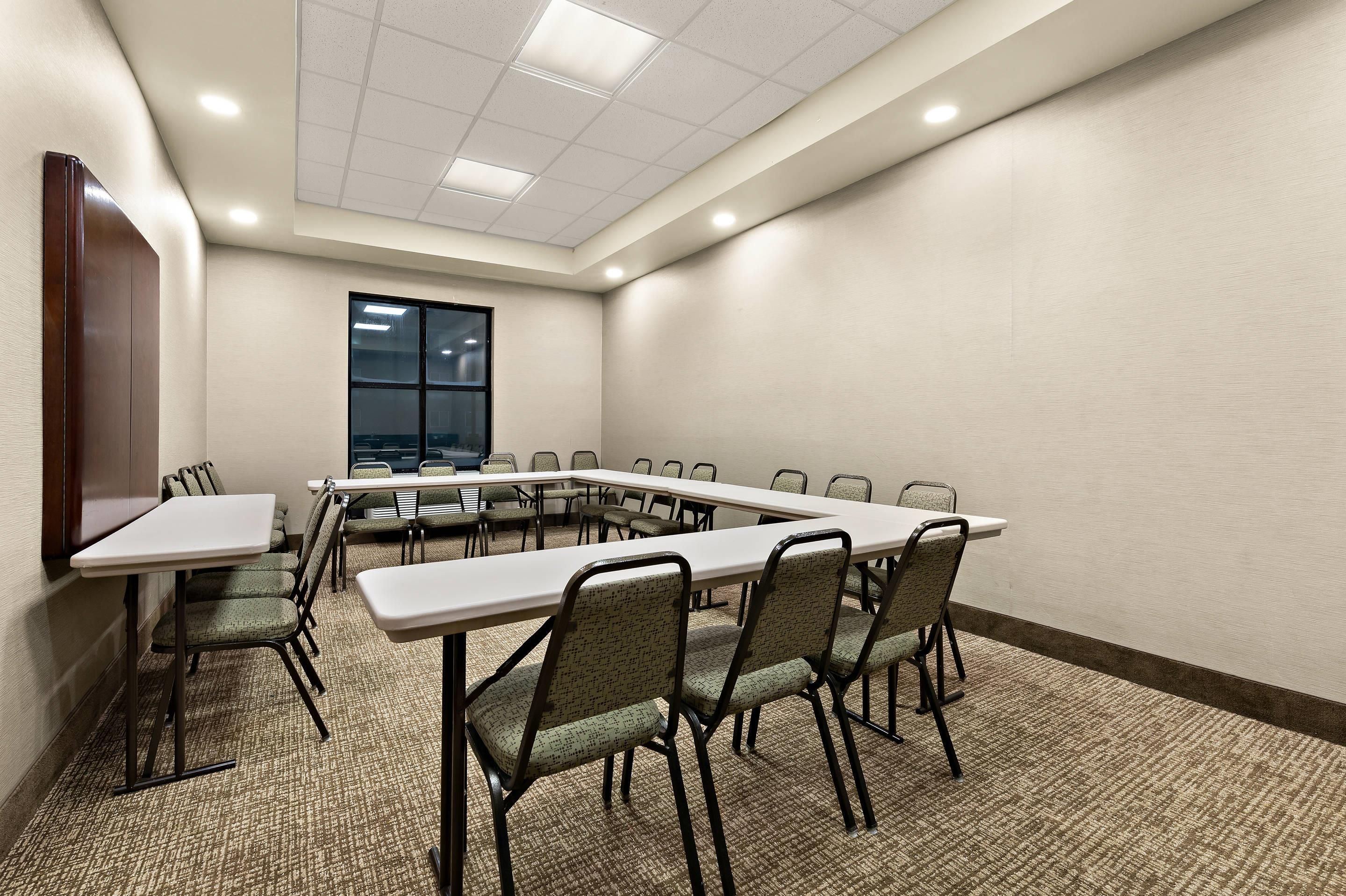 Un salón de conferencias con una larga mesa, sillas, piso alfombrado y ventana con persianas.
