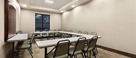 Un salón de conferencias con una larga mesa, sillas, piso alfombrado y ventana con persianas.