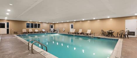An indoor swimming pool with clear water, surrounded by lounge chairs and a table.
