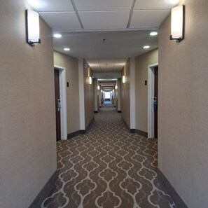 Pasillo de hotel con alfombra estampada, iluminación empotrada y puertas a ambos lados.