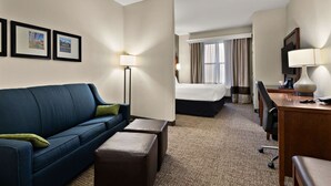 Een hotelkamer met een blauwe bank, een bed, een bureau met een lamp en ingelijste foto's aan de muur.