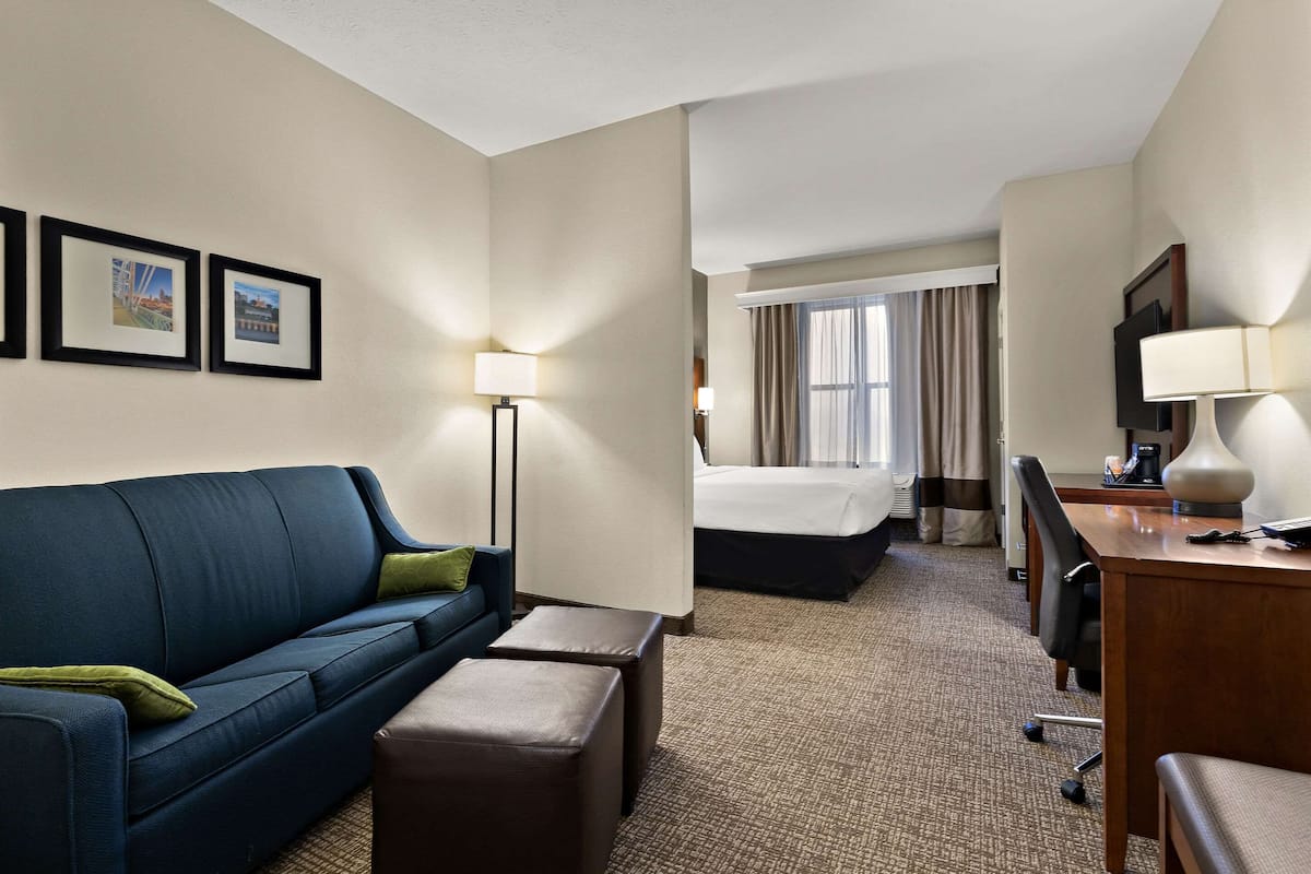 Een hotelkamer met een blauwe bank, een bed, een bureau met een lamp en ingelijste foto's aan de muur.