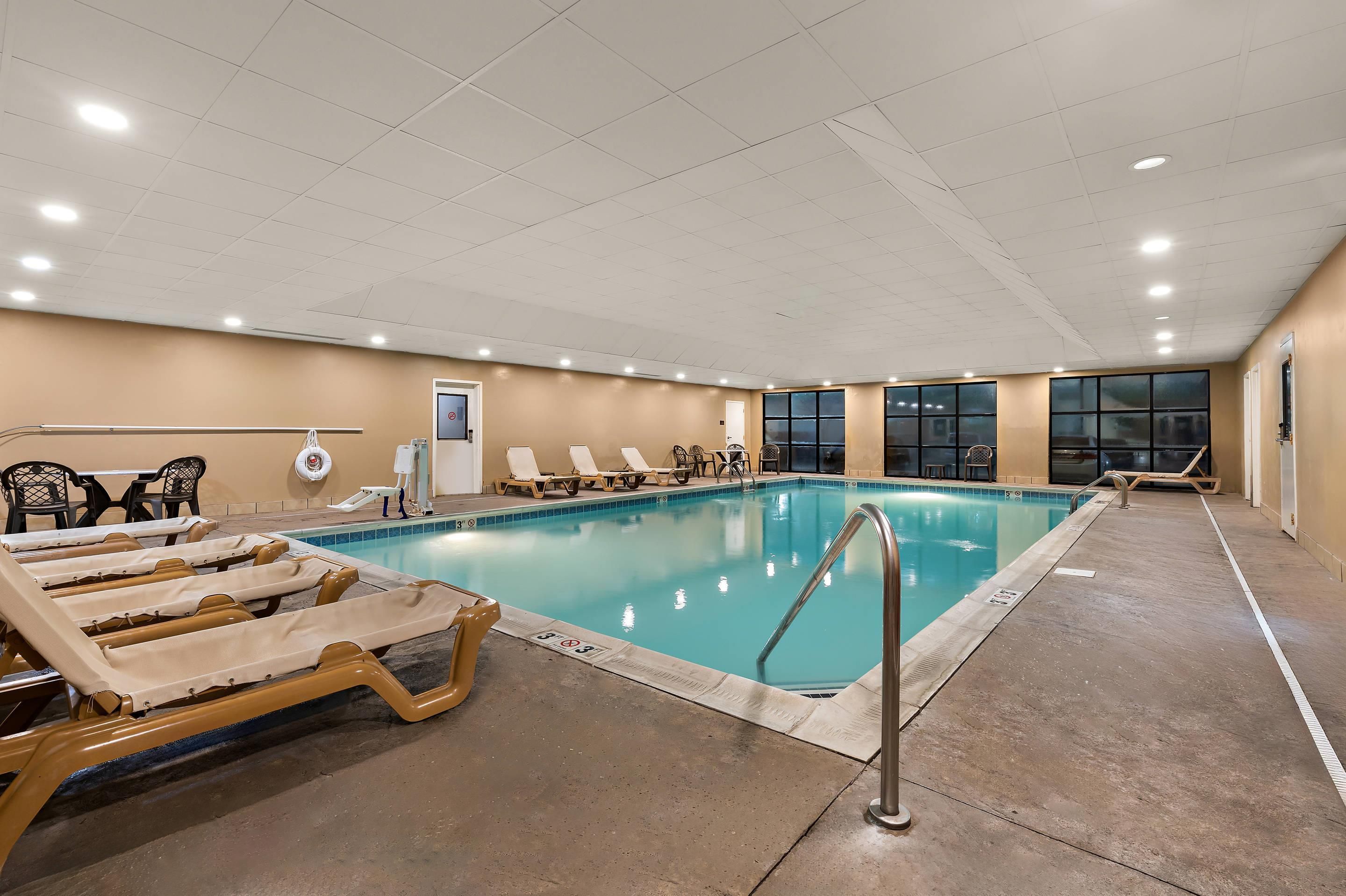 An indoor swimming pool with lounge chairs, a lifeguard stand, and a clear view of the outside through large windows.
