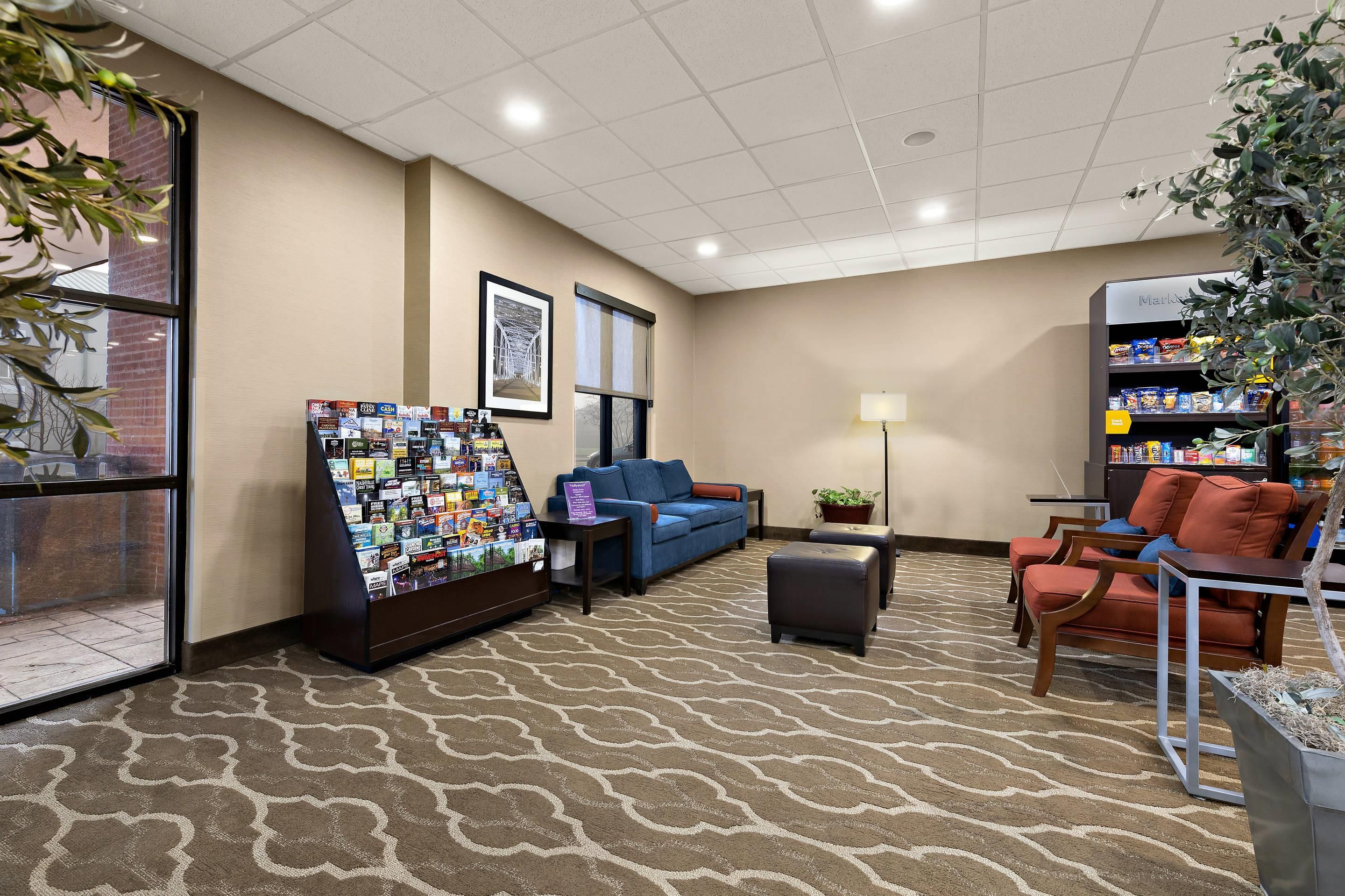 A lobby area with a seating arrangement, a magazine rack, a framed picture on the wall, and a vending machine.