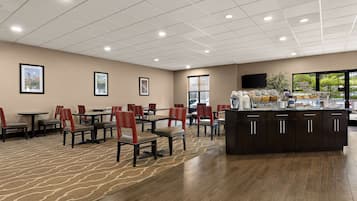 A spacious dining area with multiple tables and chairs, a central counter with a coffee station, and framed artwork on the walls.