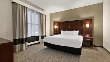 Una habitación de hotel con una cama grande, dos mesitas de noche, una lámpara de pared y cortinas en la ventana.