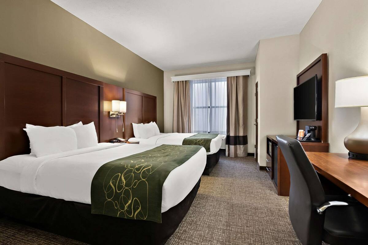 Een hotelkamer met twee bedden, een bureau, een televisie en een raam met gordijnen.