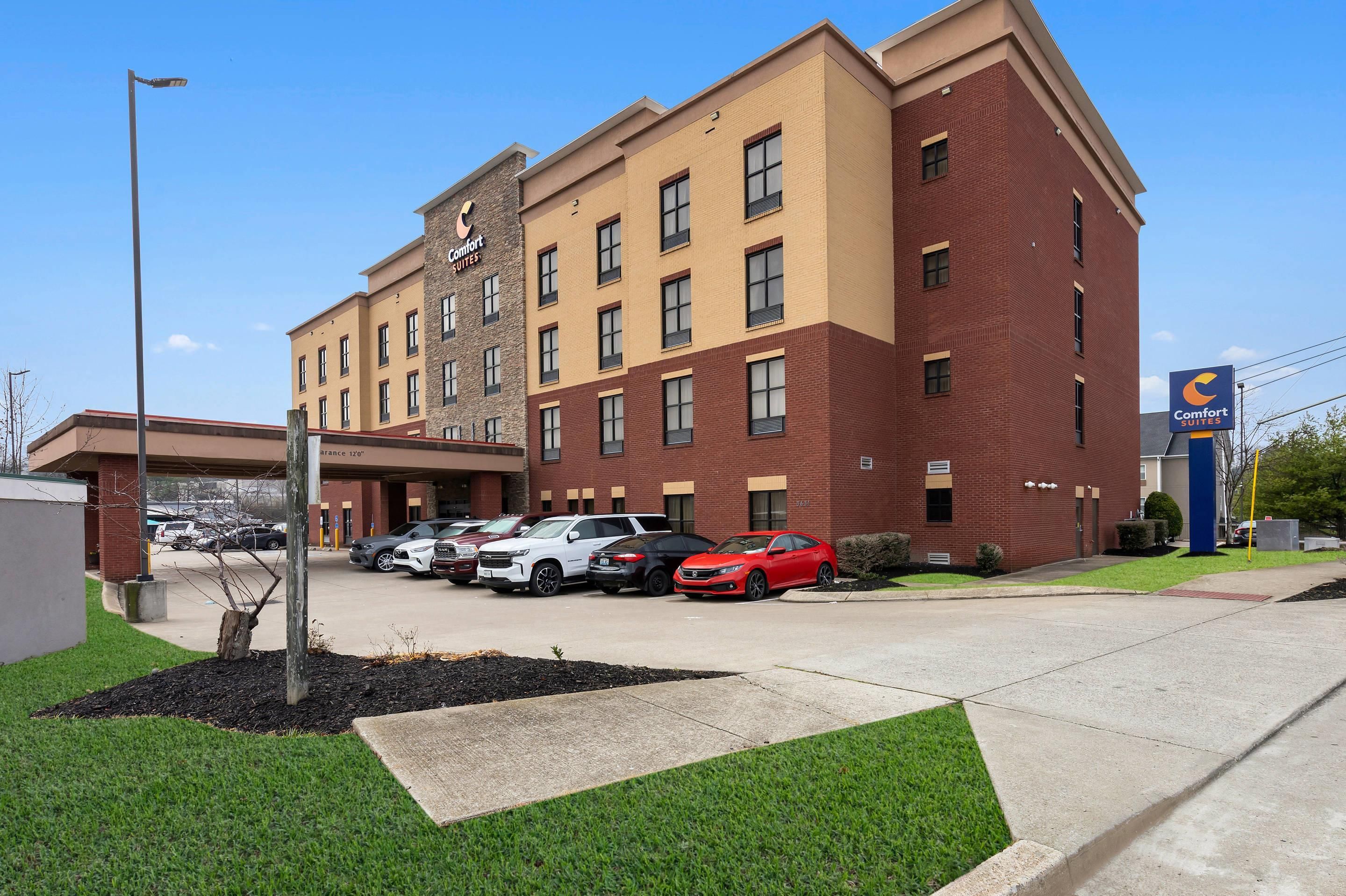 Un hotel con fachada de ladrillo, varias ventanas y un estacionamiento con varios coches.