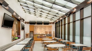 A modern restaurant with a high ceiling, multiple tables and chairs, and a kitchen area in the background. - Fairfield by Marriott New York Manhattan Times Square (New York)