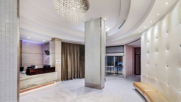 A modern hotel lobby with a reception desk, a large chandelier, a seating area, and a view of the outside. - Fairfield by Marriott New York Manhattan Times Square (New York)