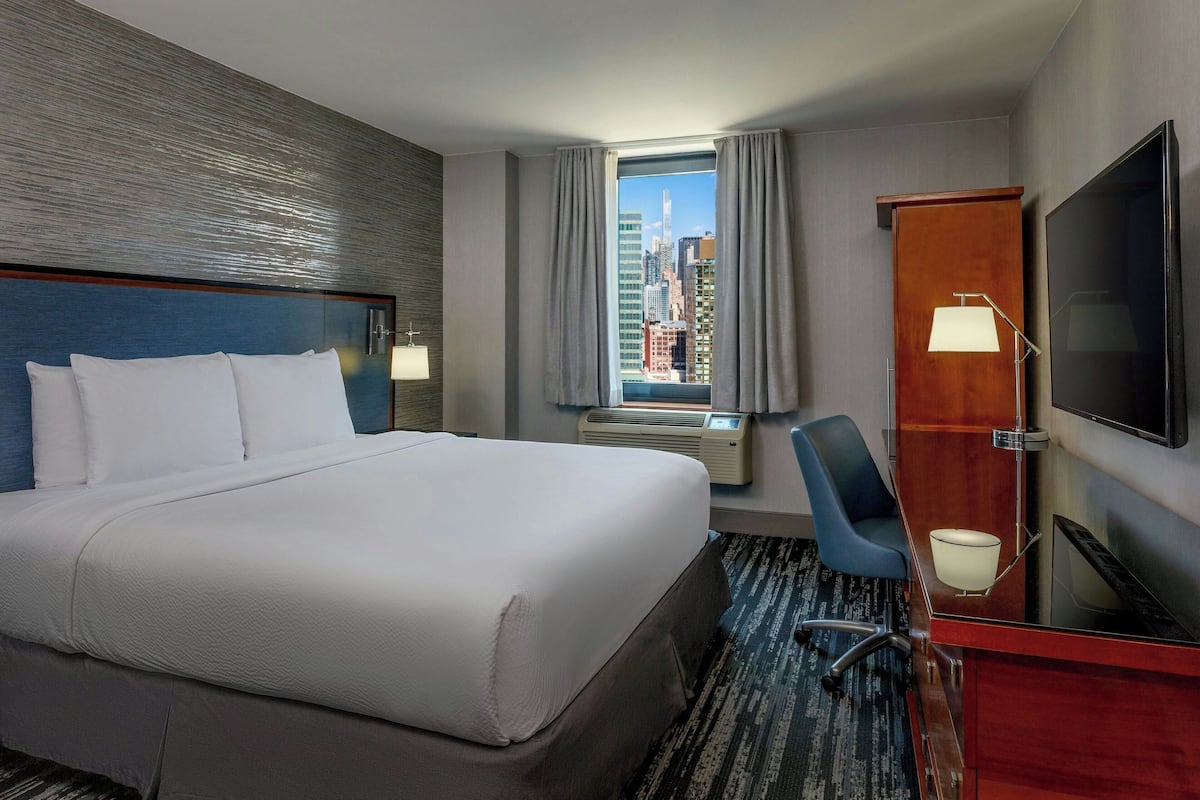 Una habitación de hotel con una cama grande, un escritorio con una silla, un televisor y una ventana con vistas a la ciudad.