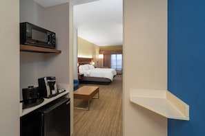 A hotel room with a bed, a desk with a coffee maker, a microwave, and a TV on a shelf. - Holiday Inn Express Hotel & Suites Talladega by IHG (Talladega)