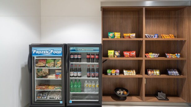 A vending machine with frozen food and cold beverages, and a wooden shelf unit with snacks and packaged goods. - Holiday Inn Express Hotel & Suites Talladega by IHG (Talladega)