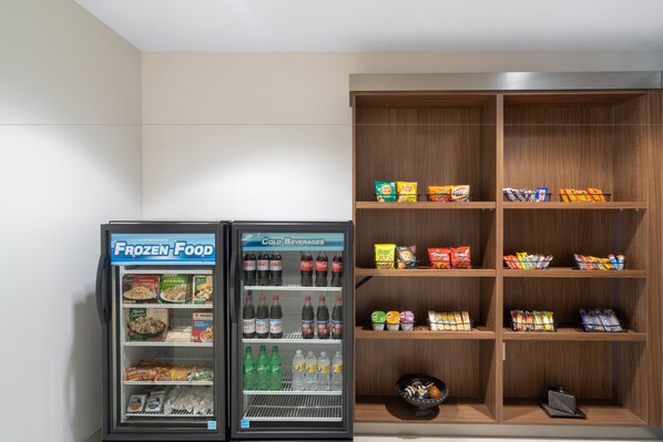 Un distributeur automatique proposant des aliments surgelés et des boissons fraîches, ainsi qu’une étagère en bois contenant des collations et des produits emballés.