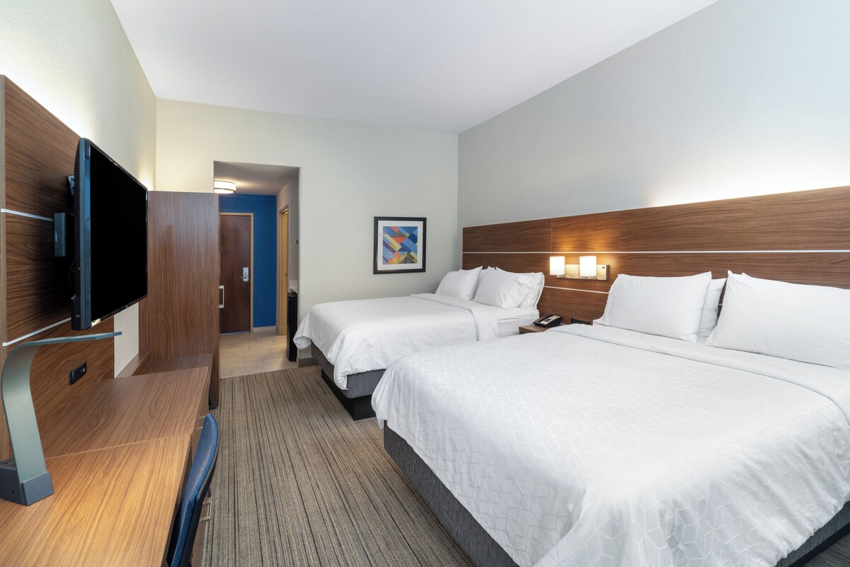 A hotel room with two beds, a desk with a flat-screen TV, a wooden headboard, and a framed picture on the wall.