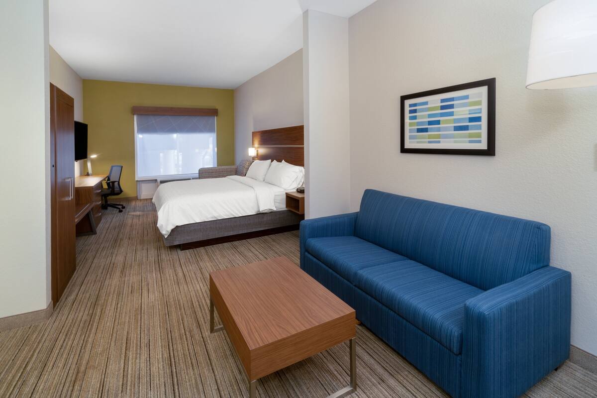 Une chambre d’hôtel avec un lit, un canapé bleu, une table basse en bois, un bureau avec une chaise et un téléviseur fixé au mur.