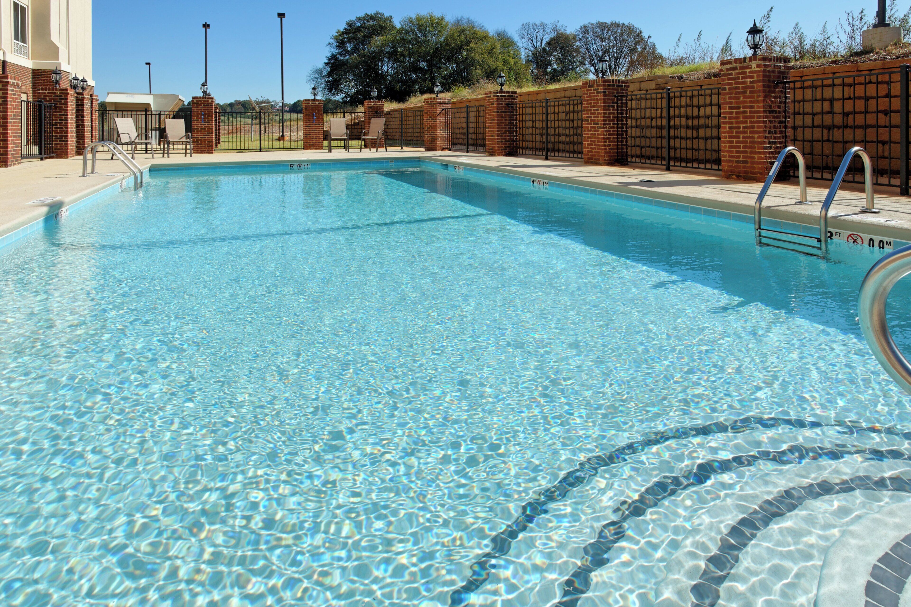 A clear swimming pool with a brick wall and metal railings.