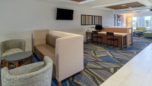 A hotel lobby with a sofa, chairs, a small table, a reception desk, and a TV. - Holiday Inn Express Hotel & Suites Talladega by IHG (Talladega)