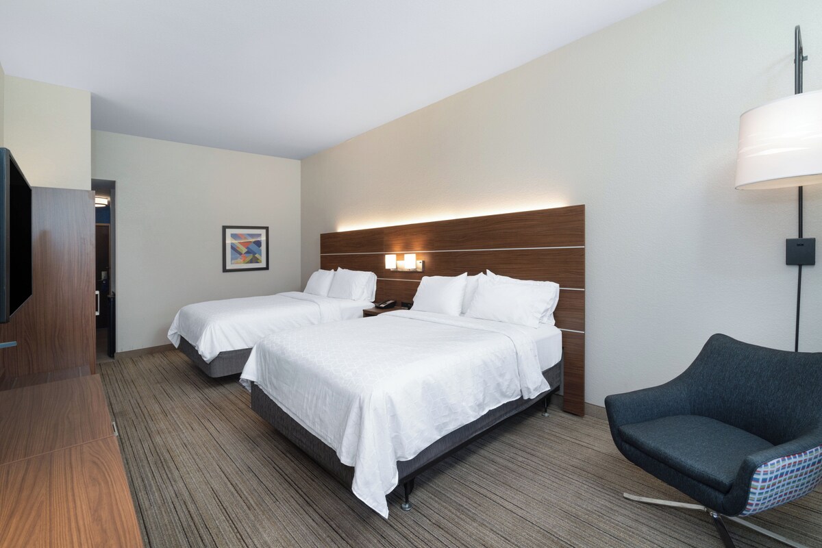 A hotel room with two beds, a TV, a desk, and a chair.