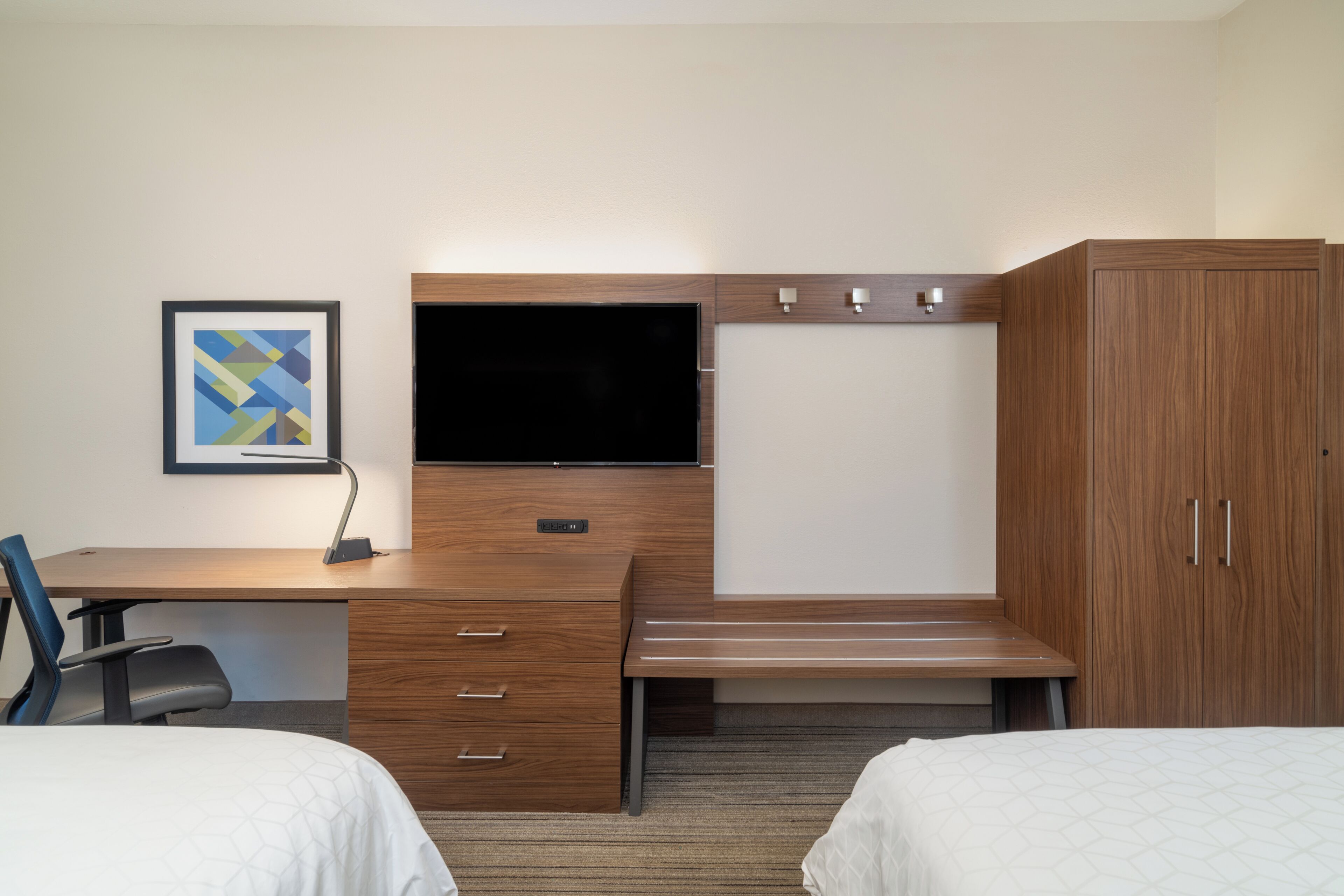 Habitación de hotel con escritorio de madera, televisión de pantalla plana, cama y armario.