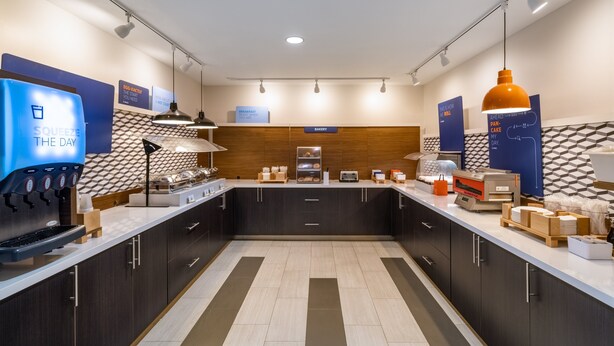 A modern kitchen area with a coffee machine, a bakery section, and a breakfast bar. - Holiday Inn Express Hotel & Suites Talladega by IHG (Talladega)