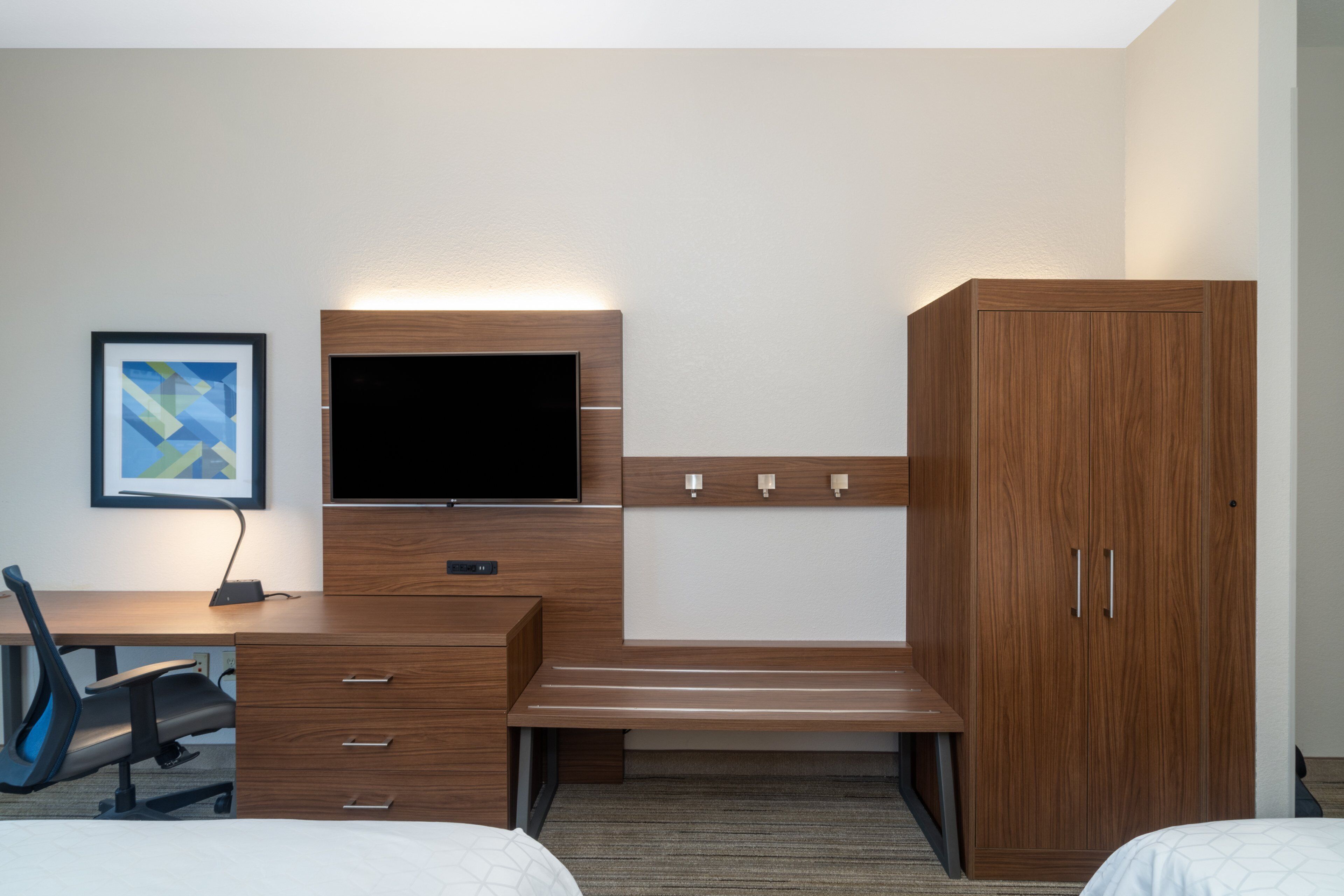 Une chambre d’hôtel équipée d’un bureau en bois, d’un téléviseur à écran plat, d’un lit et d’une armoire.