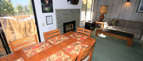 A dining area with a wooden table and chairs, a fireplace, a sofa, and a TV mounted on the wall.