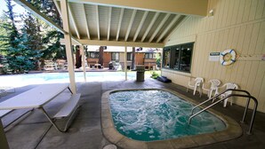Et overdækket poolområde med jacuzzi, picnicbord og hvide stole.