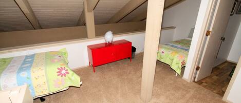Une chambre avec un plafond en pente, une commode rouge, deux lits avec une literie à motifs floraux et une chaise en bois.