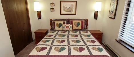 A bedroom with a large bed, two bedside tables, a wooden wardrobe, and a window with blinds.