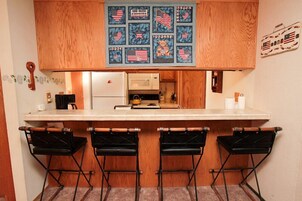 A kitchen with wooden cabinets, a white countertop, and a bar area with three black stools.