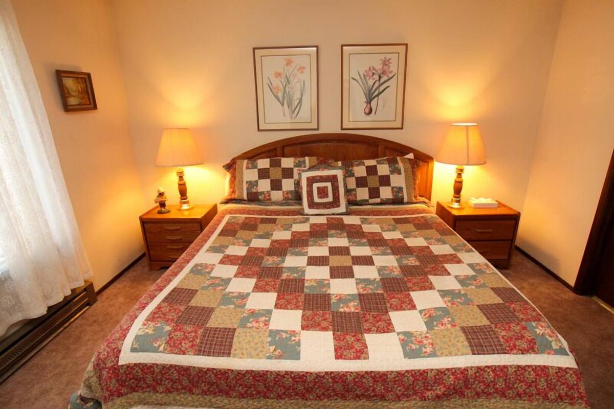 Una cama bien hecha con colcha floral, dos lámparas de noche y un cuadro con motivos florales en la pared.