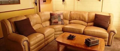 A living room with a brown leather sectional sofa, a wooden coffee table, and a fireplace.