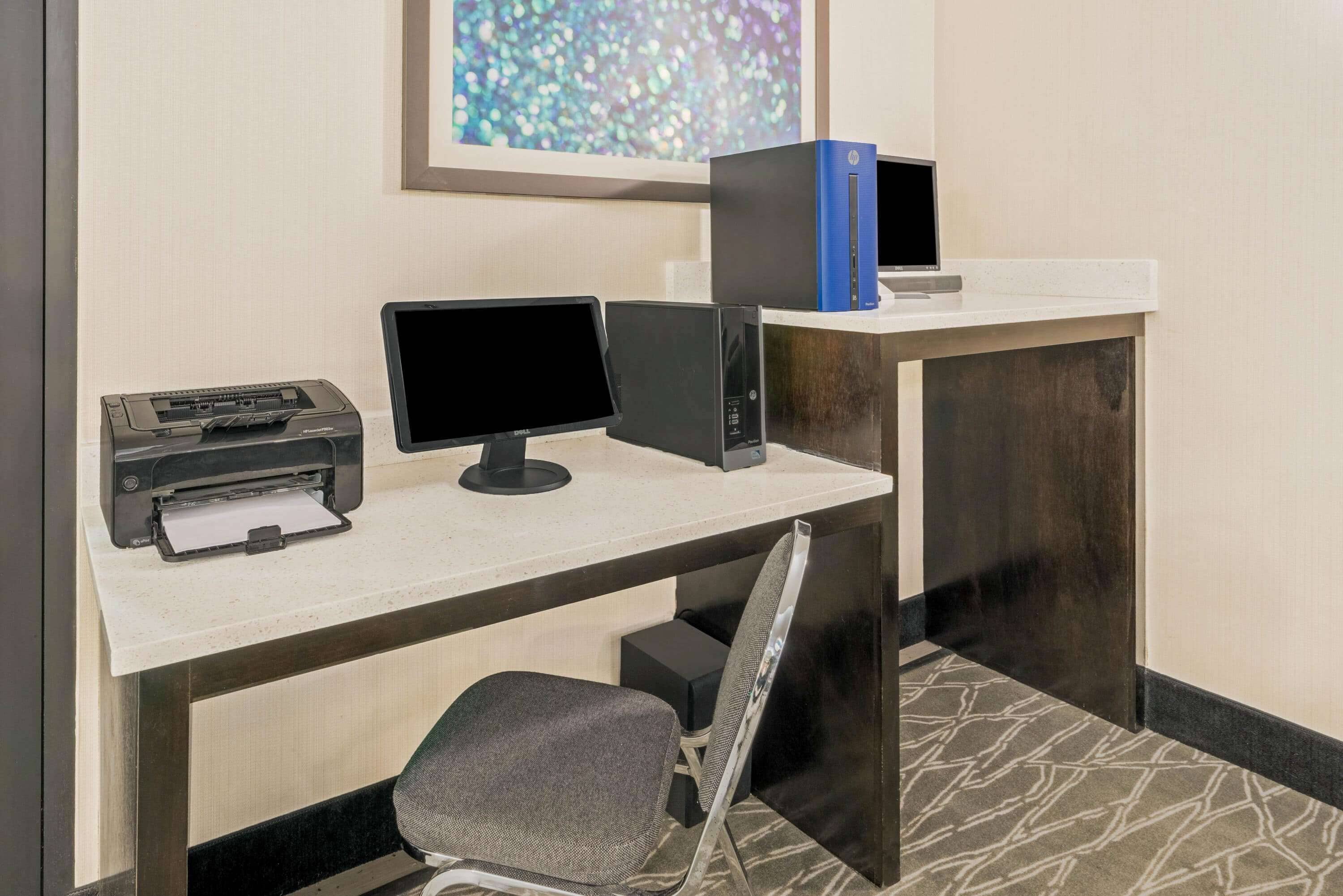 A hotel reception desk with a printer, two monitors, a computer, and a chair.