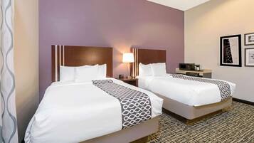 Habitación de hotel con dos camas, una mesita de noche con lámpara, una pequeña mesa con microondas y cuadros en la pared.