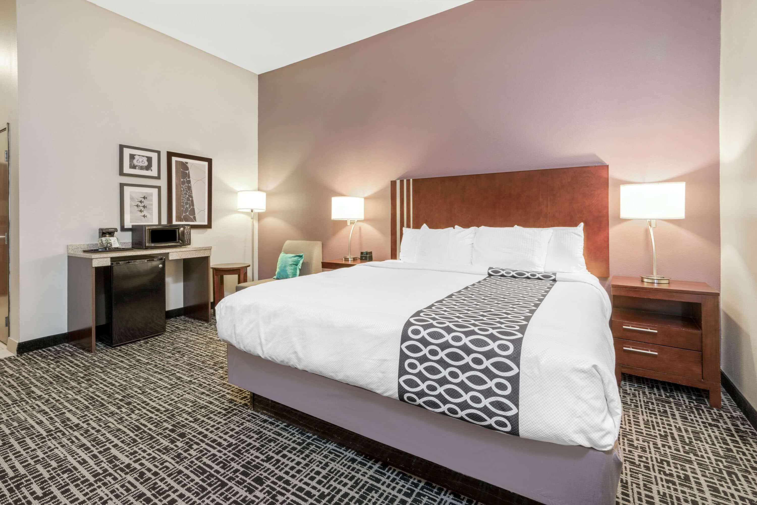 A hotel room with a large bed, bedside tables, a desk with a computer, and wall-mounted lamps.