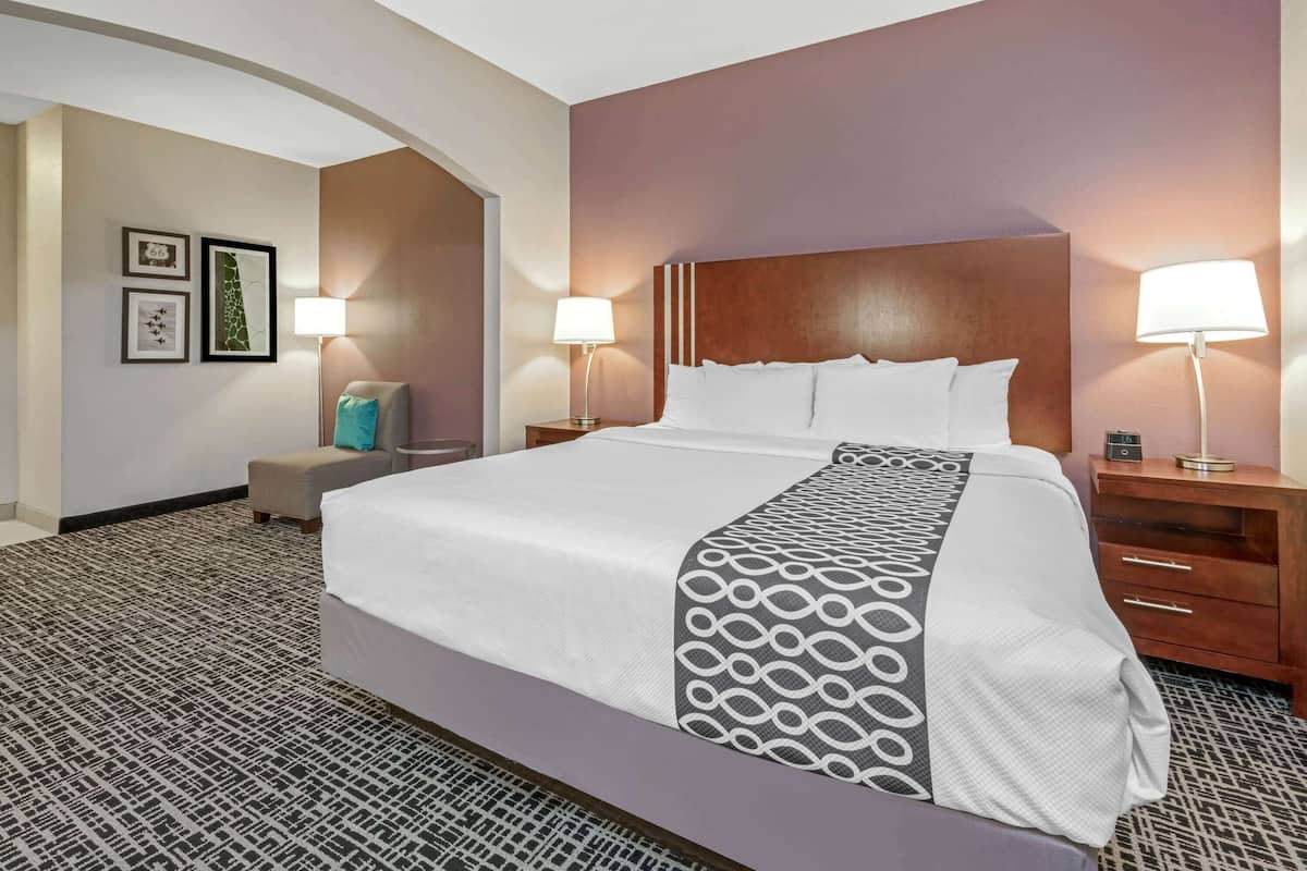 A hotel room with a large bed, two bedside tables, a nightstand, a chair, and a patterned carpet.