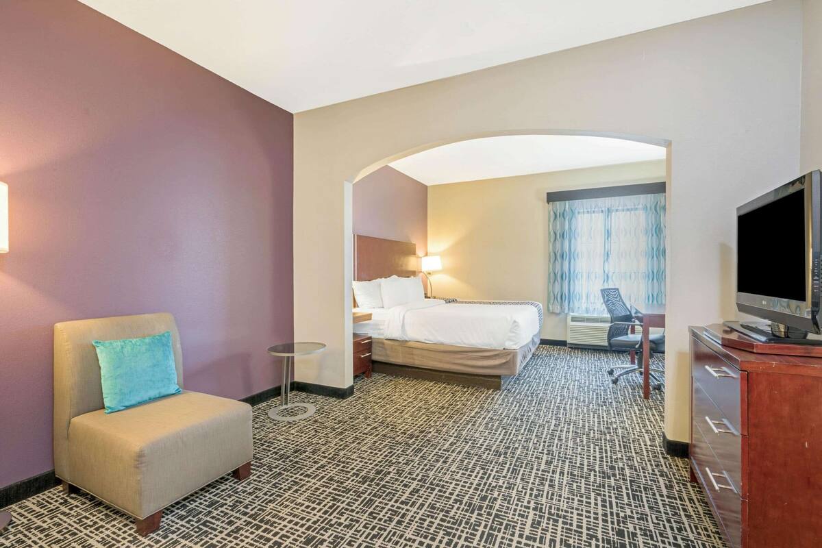 A hotel room with a bed, a chair, a TV, and a desk.