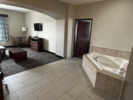 Habitación de hotel con una bañera grande, un escritorio con silla, un televisor y una puerta.