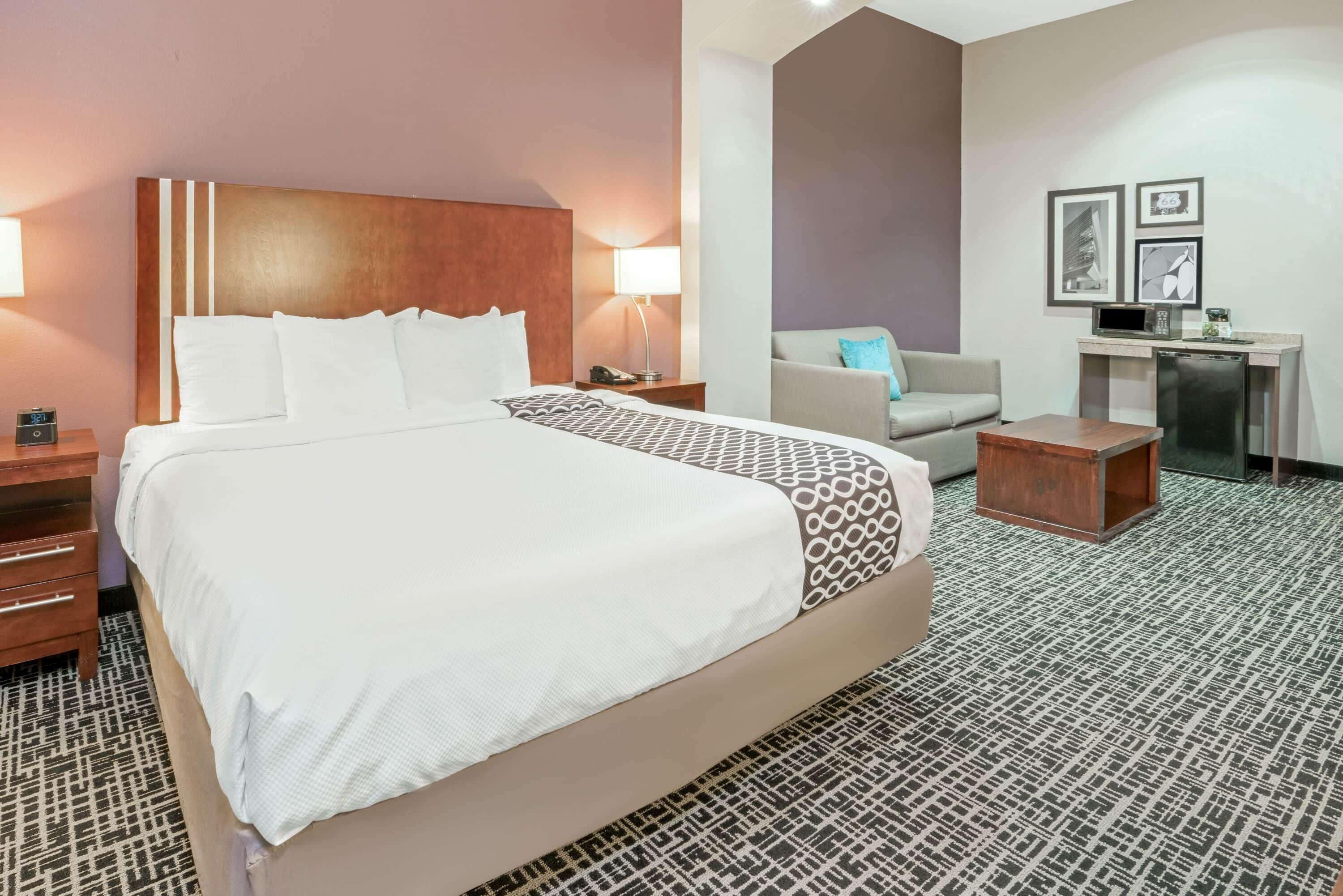 A hotel room with a large bed, bedside tables, a desk, a chair, and a small kitchenette.