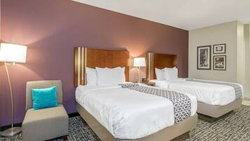 A hotel room with two beds, a chair, and a nightstand with lamps.