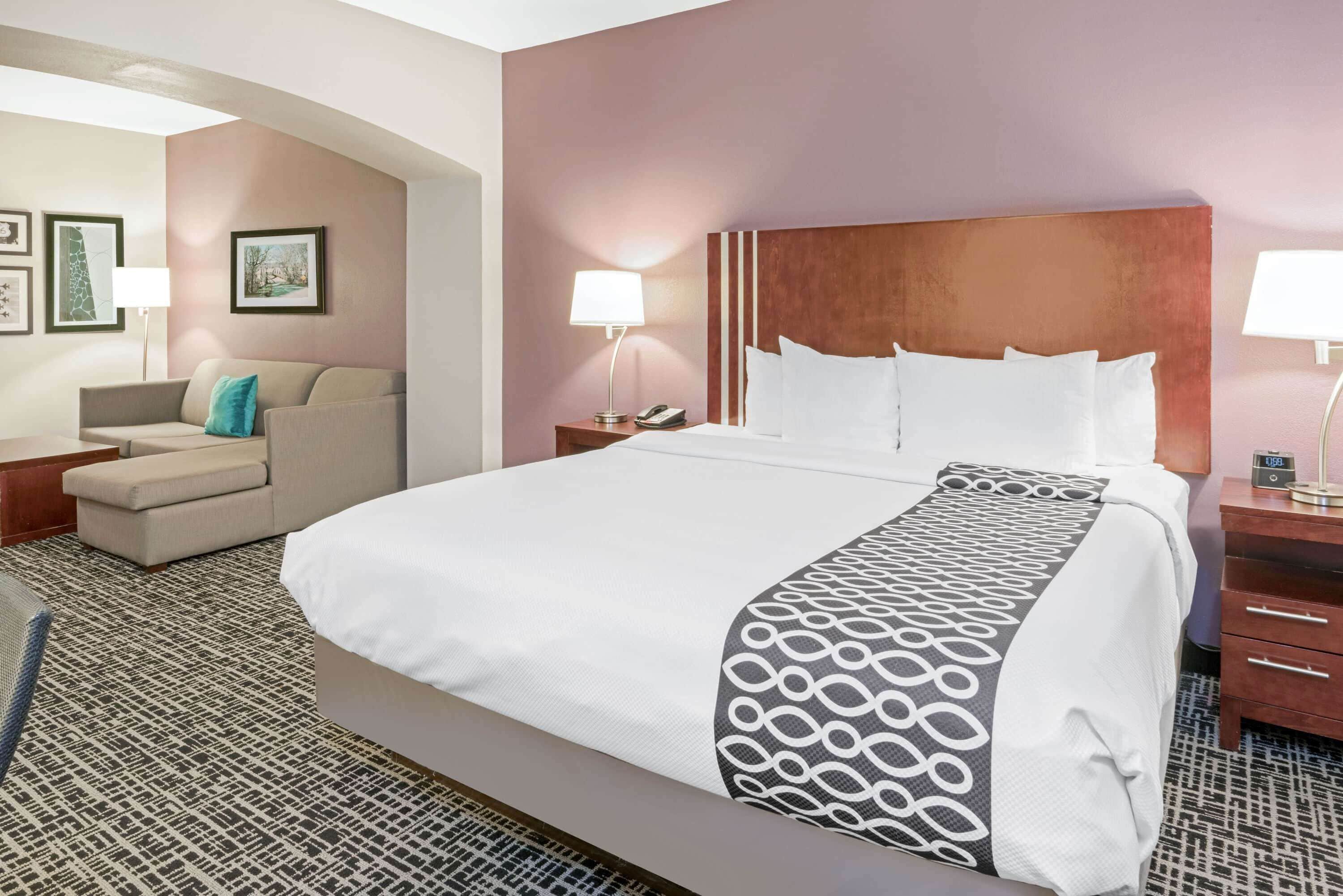 A hotel room with a large bed, a sofa, a nightstand with a lamp, and framed pictures on the wall.
