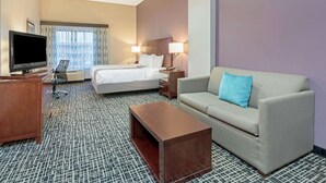 A hotel room with a bed, a sofa, a TV, a desk, and a patterned carpet. - La Quinta Inn & Suites by Wyndham Oklahoma City -Yukon (Yukon)