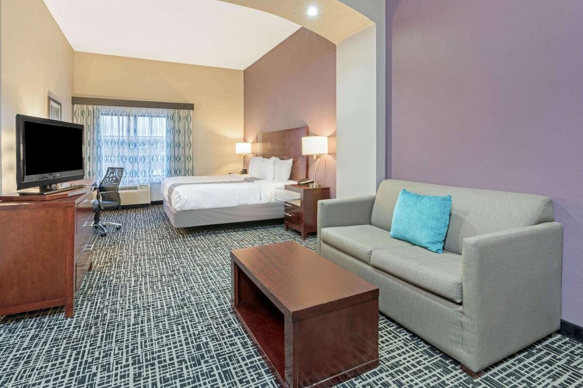 A hotel room with a bed, a sofa, a TV, a desk, and a patterned carpet.