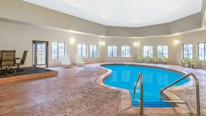 An indoor swimming pool with a curved edge, surrounded by chairs and a sunlit room with large windows. - La Quinta Inn & Suites by Wyndham Oklahoma City -Yukon (Yukon)